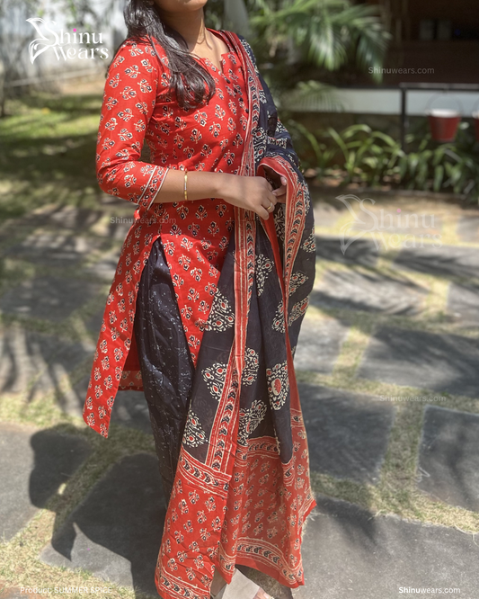 Person wearing a red and black patterned outfit with a scarf, standing outdoors.