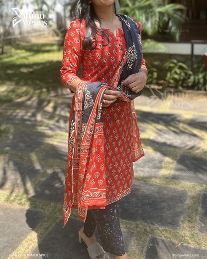 Person wearing a red patterned outfit with a black dupatta, standing outdoors.