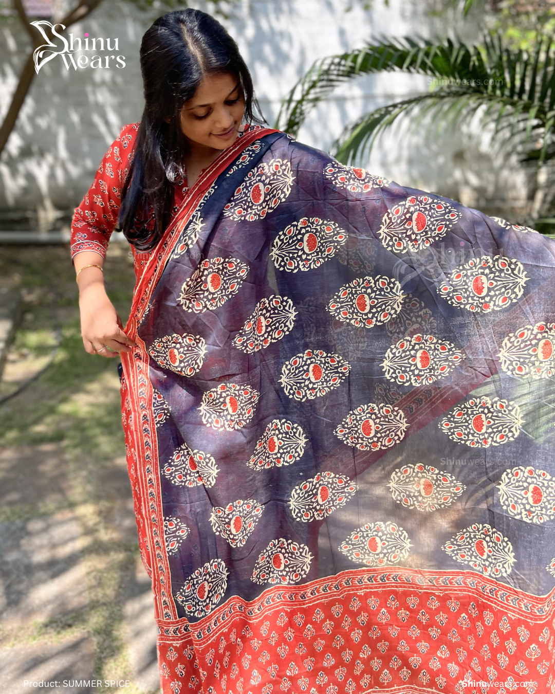 Woman wearing a blue saree with red and white patterns, standing outdoors.