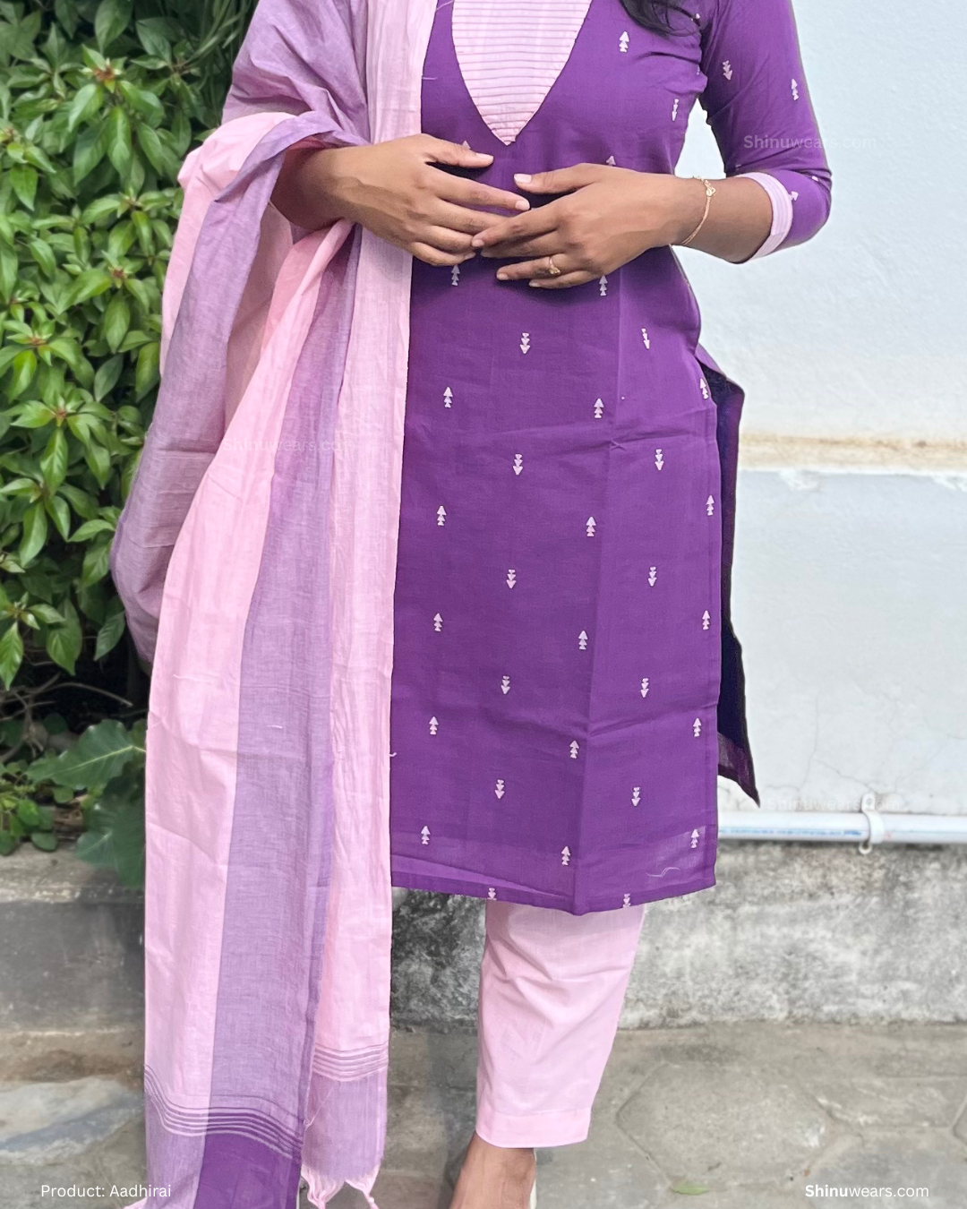 Person wearing a purple outfit with a pink dupatta against a green and gray background